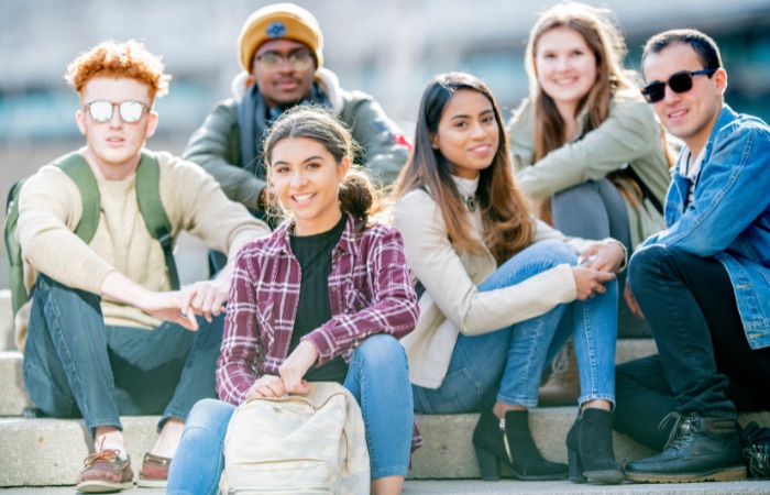Group of teens sitting on steps together, smiling at the camera.