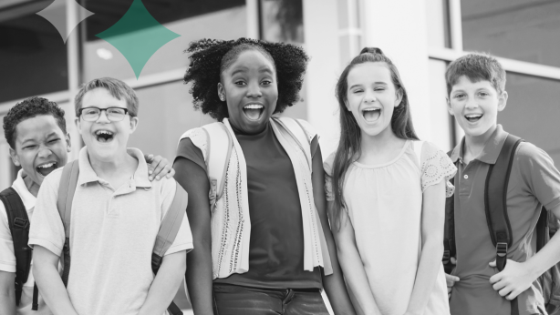 Five children, wearing backpacks, stand in front of a building, smiling and laughing.