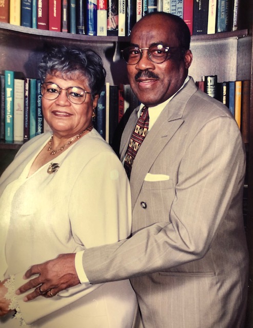 Portrait of John and Ruth Tate, standing together in front of a book case.