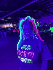 Person wearing neon hair accessories and a shirt with neon text at a glo bingo event.