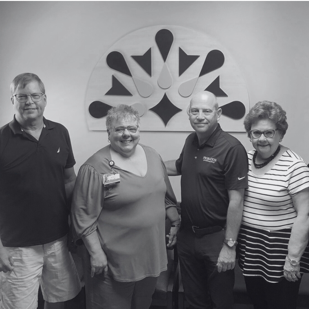 Four Clove Alliance Board Members standing and smiling in front of the organization logo.