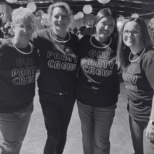 Four people wearing matching "Glo Party Crew" T-shirts pose together under hanging lights.