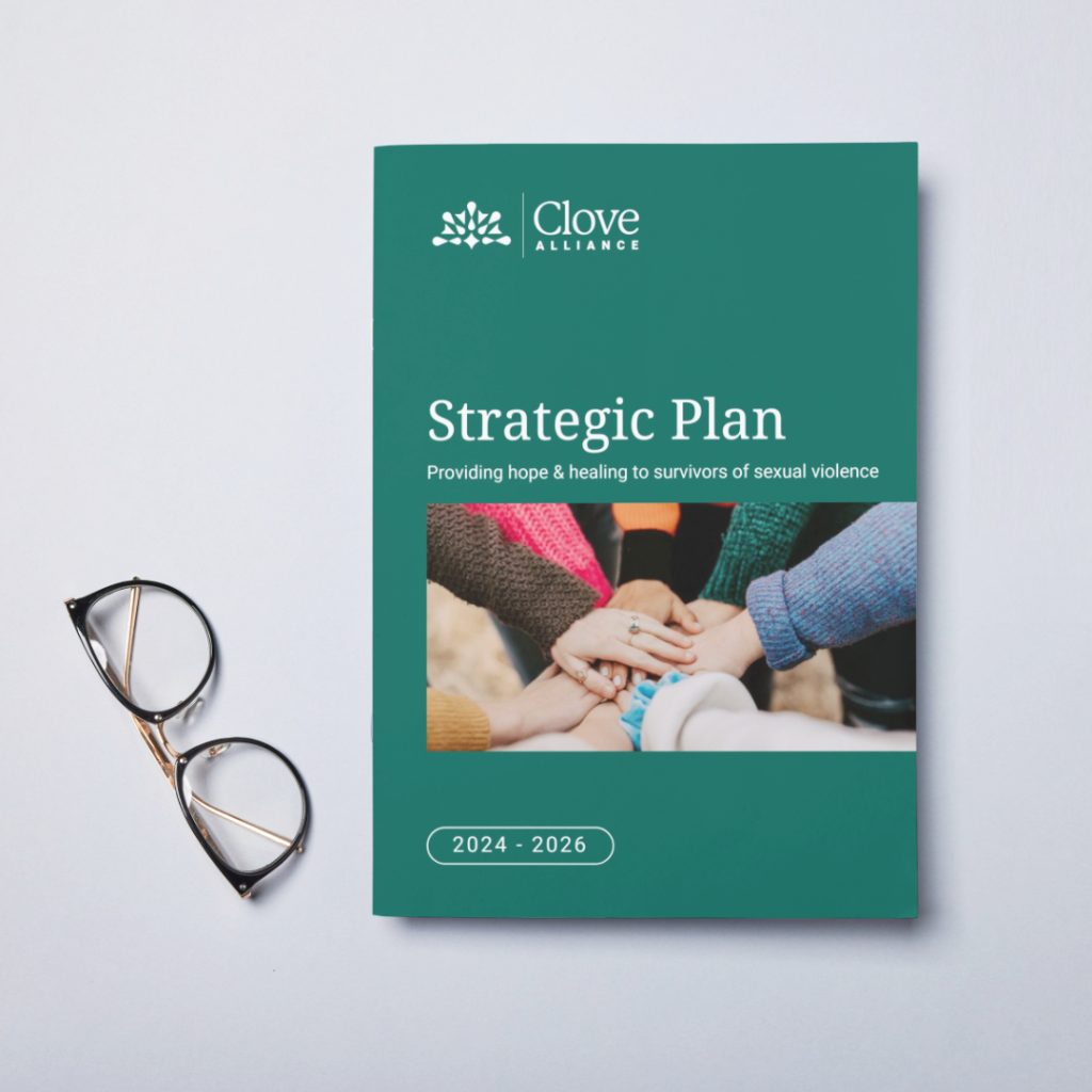 A teal document titled "Clove Alliance Strategic Plan 2024–2026" lies on a white surface next to glasses, featuring a cover photo of diverse hands stacked together.