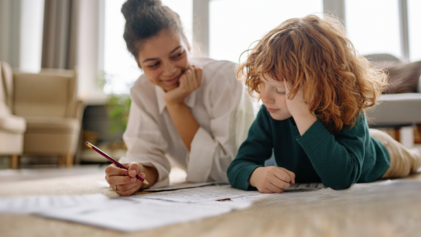 An adult and a child lie on the floor looking coloring sheets.