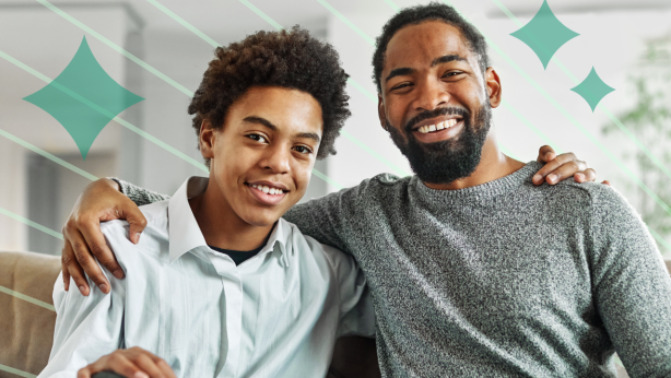 A father and son with one arm around each other's shoulders smiling together on a couch.